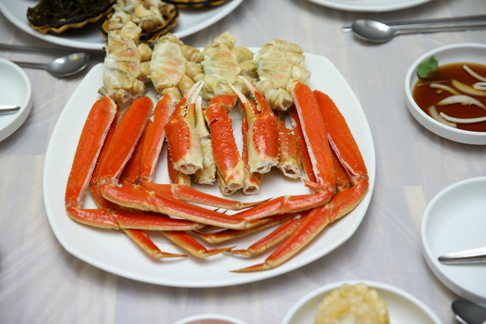 흰 접시에 쪄낸 대게 다리를 겹겹이 쌓아 담고 곁들임 그릇을 둘러 놓은 상