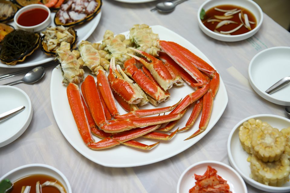 흰 접시에 쪄서 담은 대게 다리와 곁들임 그릇들이 한 상에 놓인 구성